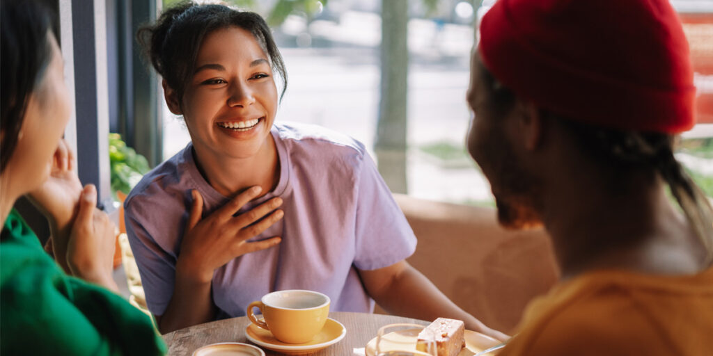 Three people sitting at a café table, smiling and talking over coffee and dessert.